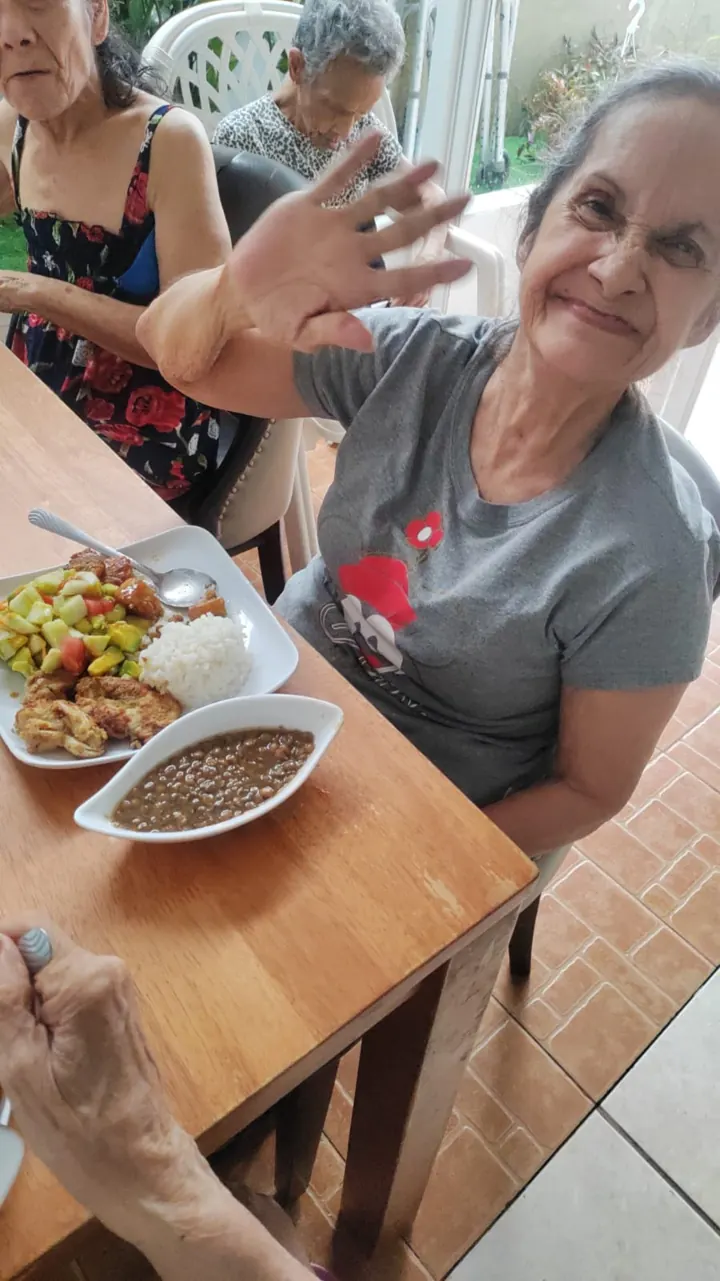 Residente saluda sonriente frente a su almuerzo: pollo, arroz, ensalada de pepino y aguacate, y lentejas.